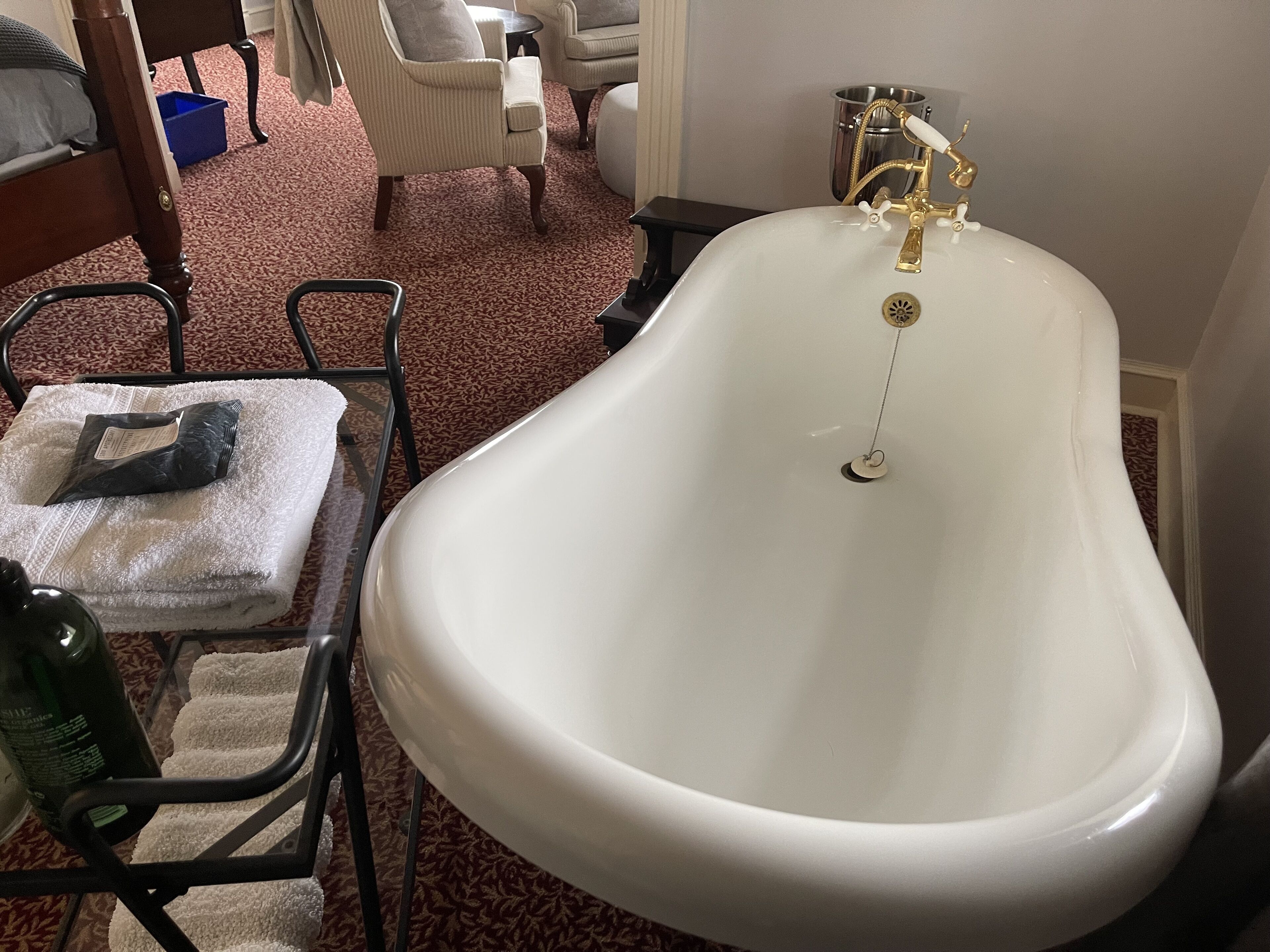 Une salle de bain avec une baignoire sur pieds, une table en verre avec une serviette et une bouteille, et une chaise.