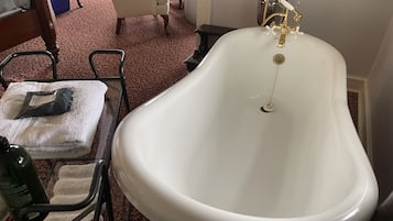 Une salle de bain avec une baignoire sur pieds, une table en verre avec une serviette et une bouteille, et une chaise.