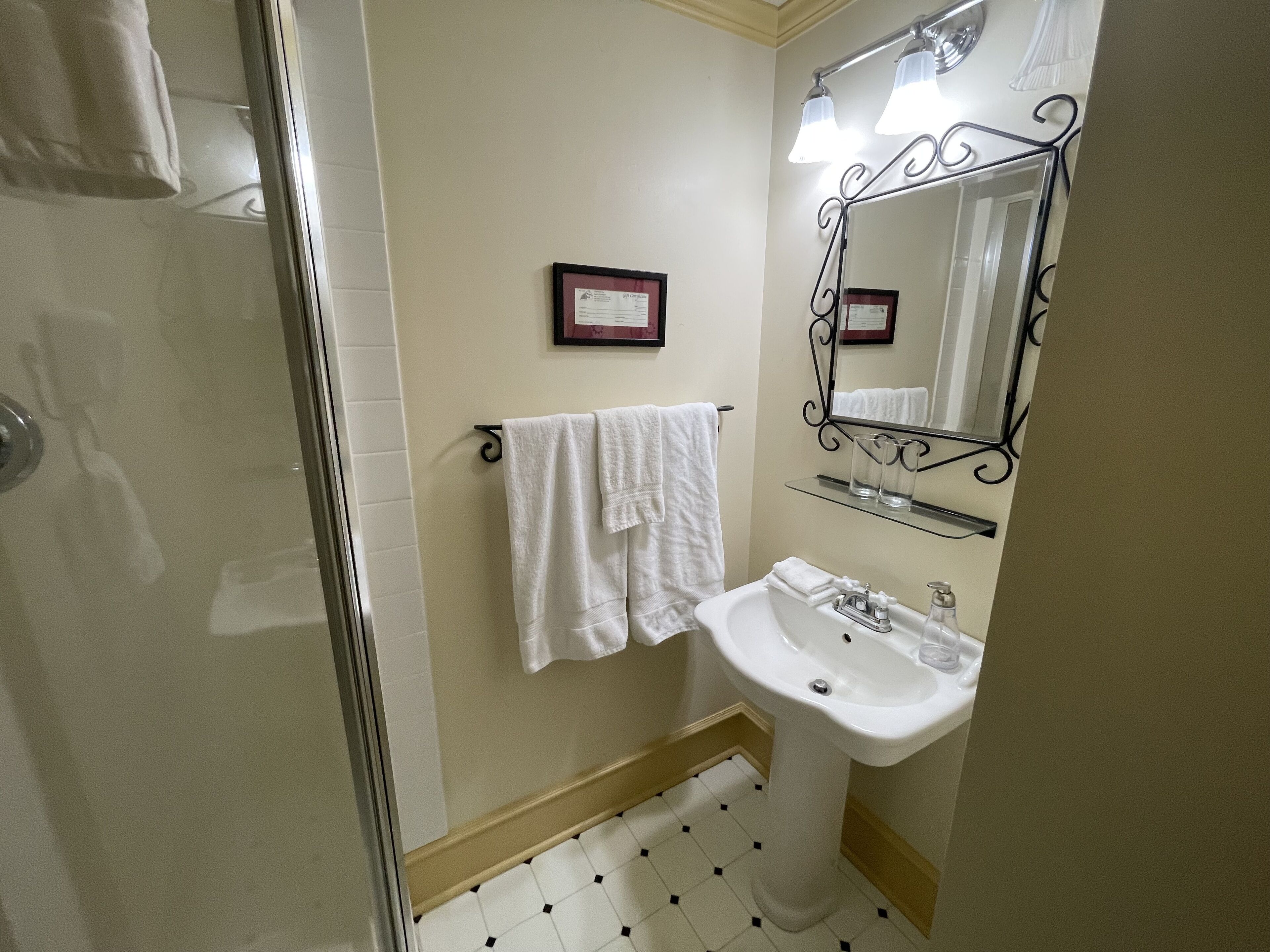 Une salle de bain avec une douche à parois de verre, un lavabo blanc avec un miroir au-dessus, et une serviette suspendue à un porte-serviettes.