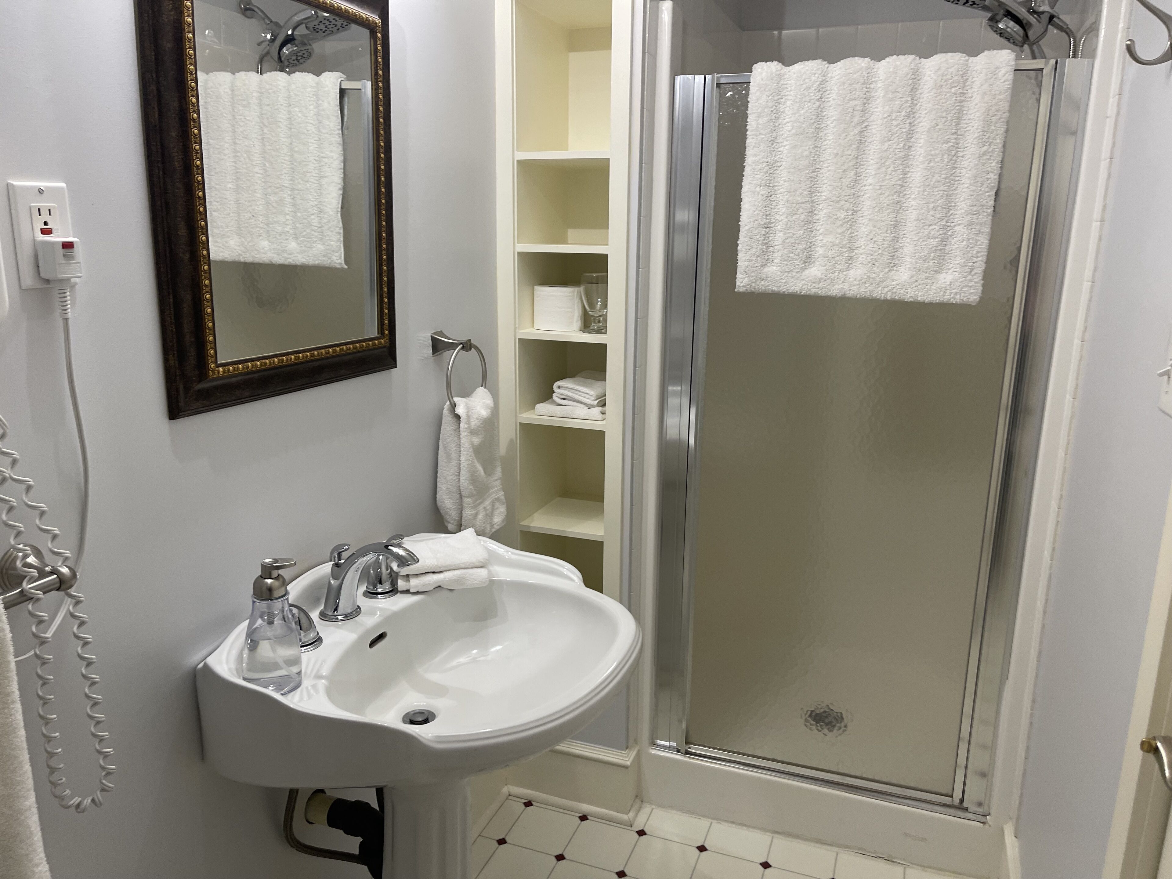 A bathroom with a white sink, a mirror, a shower with a glass door, and a towel rack.