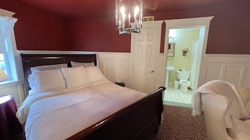 Un dormitorio con una cama de madera, ropa de cama blanca, una araña y una pared roja.