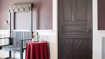 A room with a checkered floor, a dark wooden door, a red table with a white candle, and a metal coat rack.