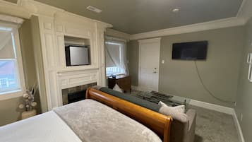 A bedroom with a bed, a television mounted on the wall, a fireplace, and a window with curtains.