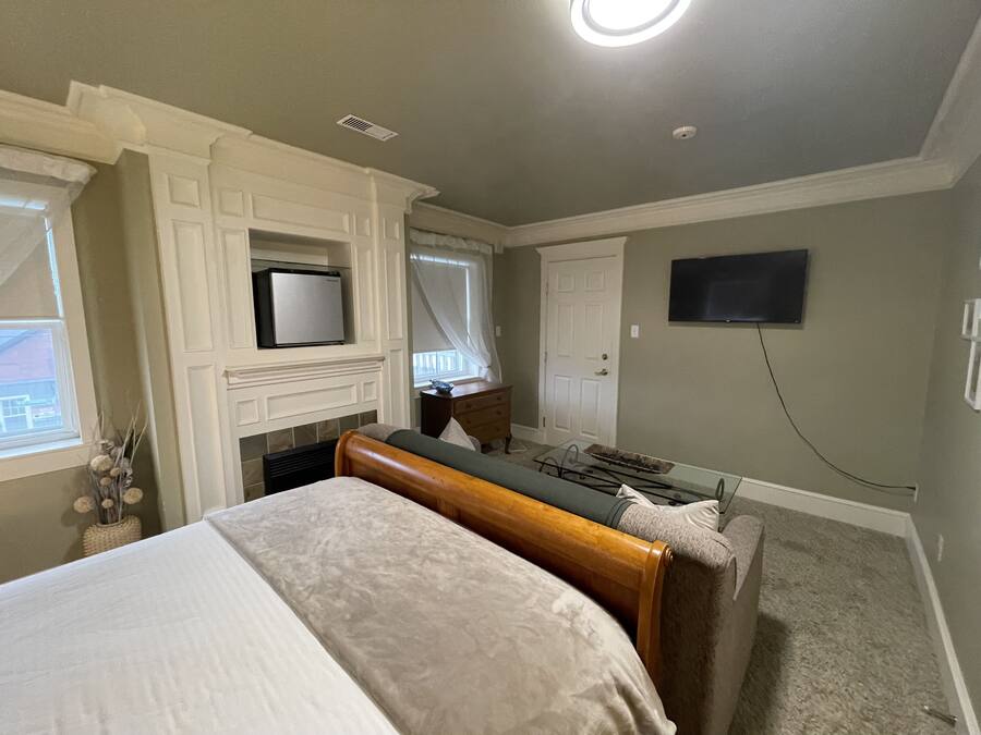 A bedroom with a bed, a television mounted on the wall, a fireplace, and a window with curtains.