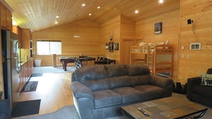 A cozy cabin interior with a leather sofa, a pool table, bunk beds, and a kitchen area.