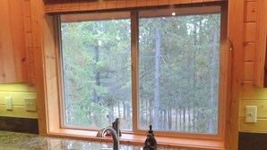 A kitchen with a granite countertop, a sink, and a window overlooking a forest. - Treetop Loft-28 miles to Yellowstone-Owner Operated (Island Park)