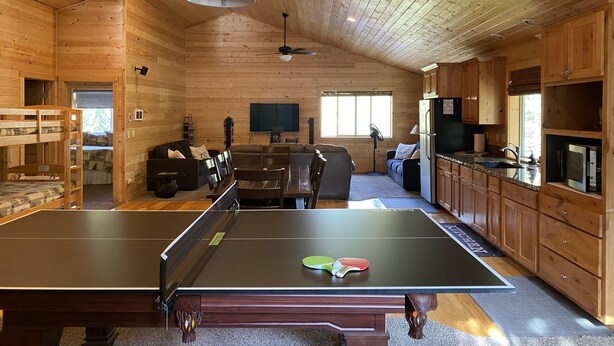 A wooden cabin interior with a ping pong table, a dining area, a kitchen, and a TV in the living room. - Treetop Loft-28 miles to Yellowstone-Owner Operated (Island Park)
