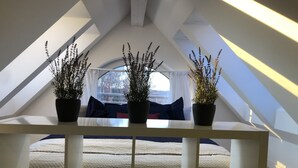 A cozy attic bedroom with a sloped ceiling, a bed with a patterned duvet, and three potted plants on a white shelf. - Luxurious country villa nestled in a horse farm on the mountain with great views (Uttenhofen)