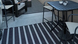 Een terras buiten met een bank, tafel en barbecueplaats, met uitzicht op een bergachtig landschap.