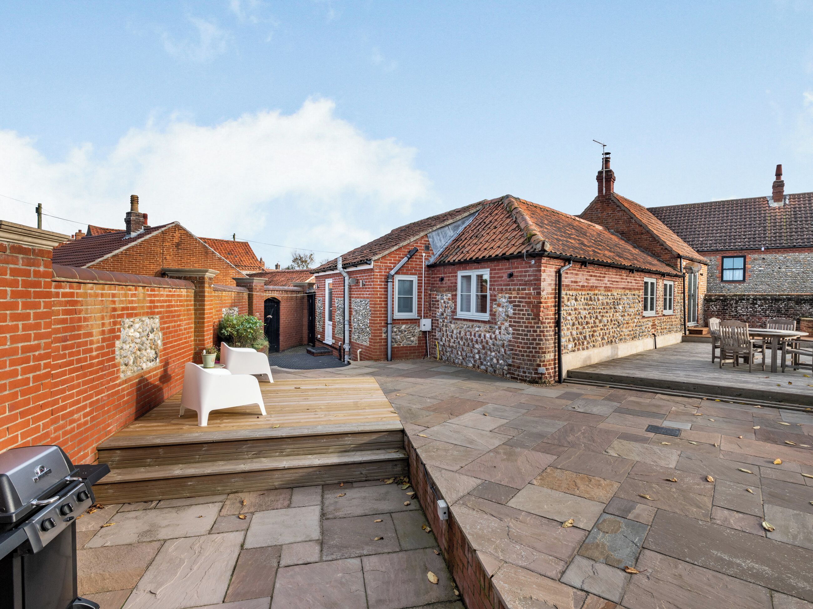 A brick house with a tiled roof, a wooden deck, and a barbecue grill.