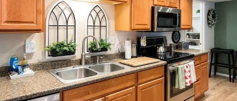 Una cocina con armarios de madera, electrodomésticos de acero inoxidable, un lavamanos doble y una ventana con plantas.