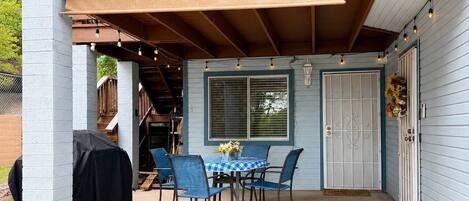 A covered patio with a table and chairs, a barbecue grill, and a door with a window.