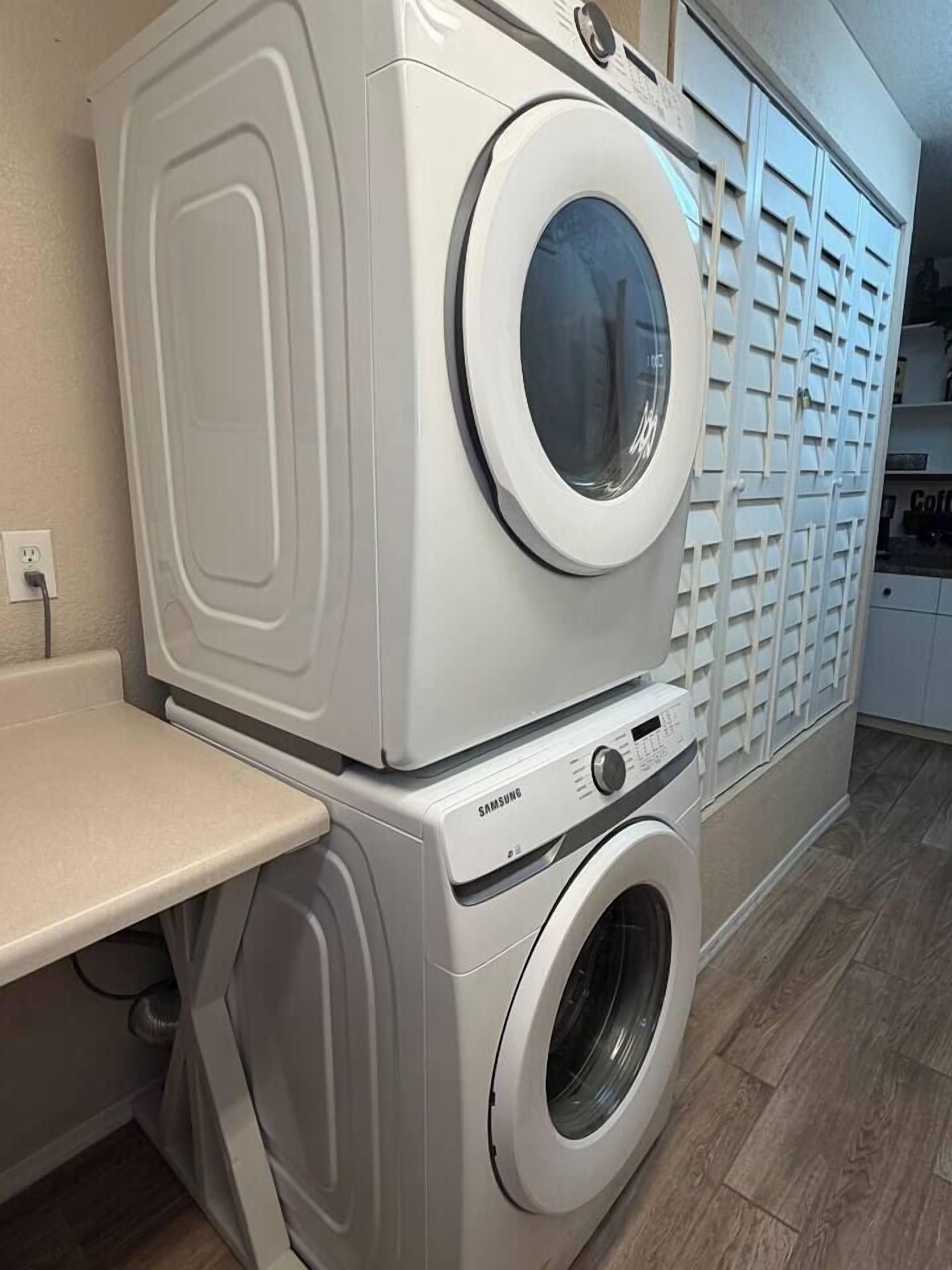 A stacked washer and dryer unit with a Samsung logo, a countertop, and a laundry basket.