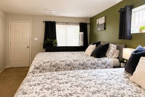 Un dormitorio con dos camas, una ventana con cortinas, una mesita de noche con lámpara y una puerta.