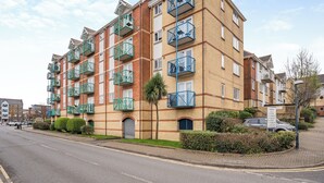 A multi-story residential building with balconies, a gated entrance, and a parking area.