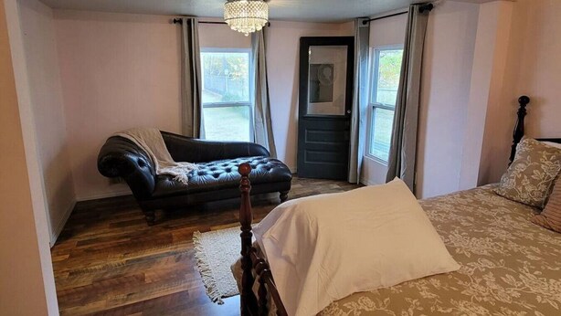 Een slaapkamer met een bed, een leren zwarte bank, een houten vloer en een kroonluchter.