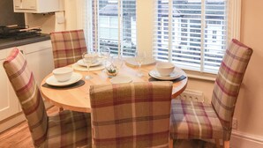 A dining area with a round table set for four, plaid chairs, and a window with blinds.