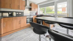 A modern kitchen with wooden cabinets, a gas stove, and a large window providing a view of the outdoors. - Academy Street Cottage (Tain)