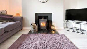 A living room with a fireplace, a sofa, a television, and a rug. - Academy Street Cottage (Tain)
