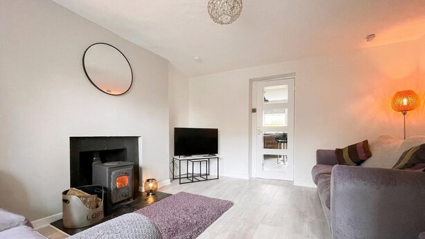 A modern living room with a fireplace, a flat-screen TV, a sofa, and a lamp. - Academy Street Cottage (Tain)
