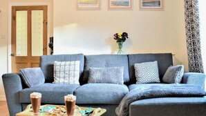 A living room with a grey sofa, a wooden coffee table with a drink and cookies, framed pictures on the wall, and a door with frosted glass panels. - 2 bedroom accommodation in Alnwick (Alnwick)