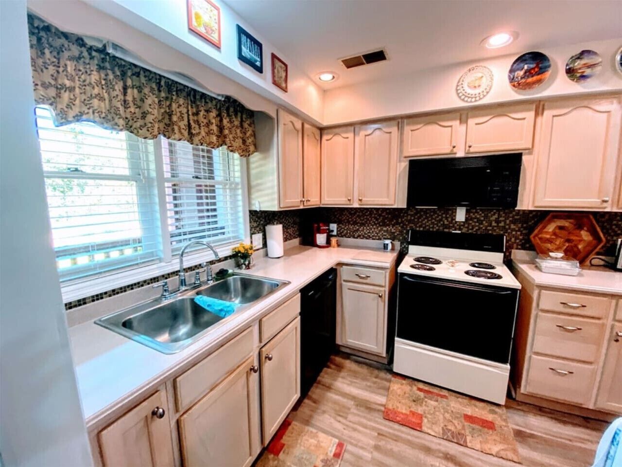 A compact kitchen with white cabinets, a black stove, and a window with blinds.