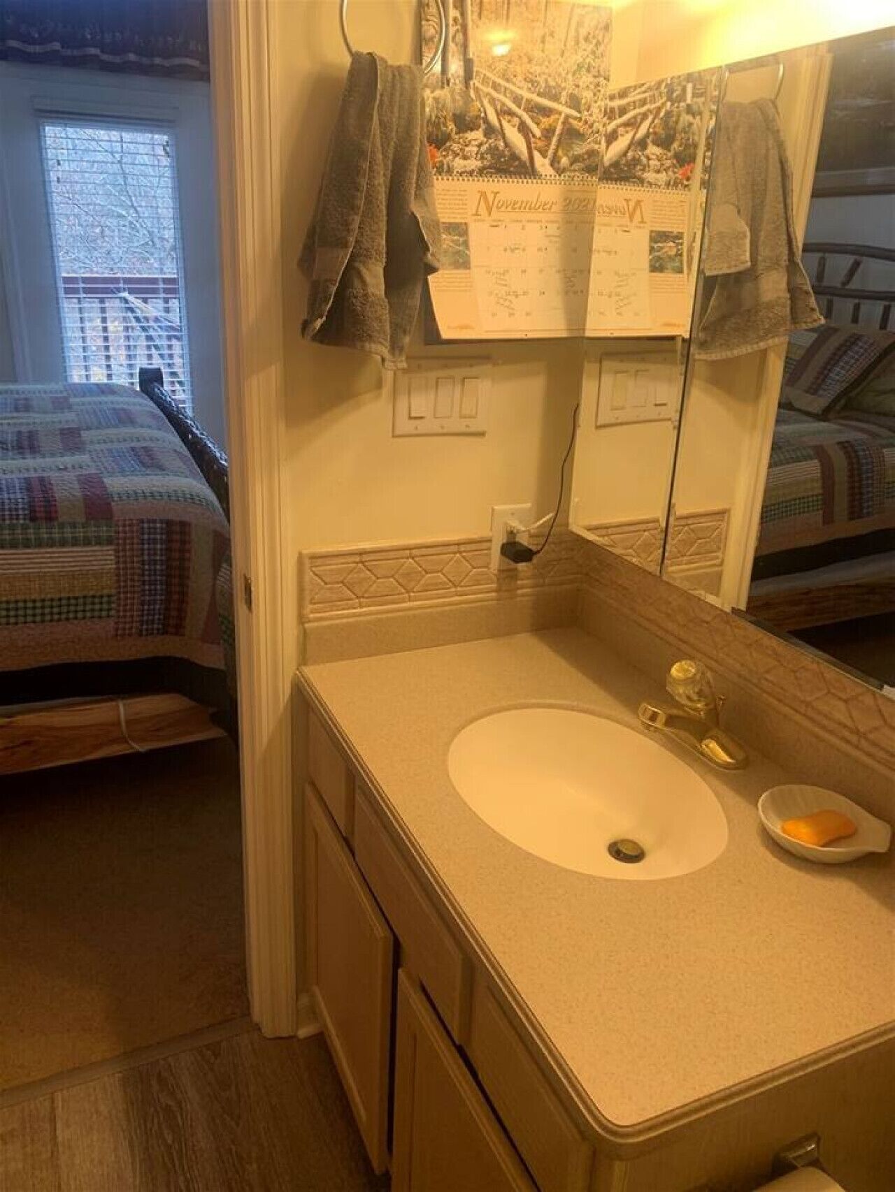 A compact bathroom with a single sink, a mirror, and a calendar on the wall.