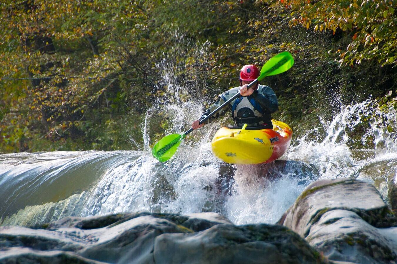 A person kayaking on a river with a waterfall.