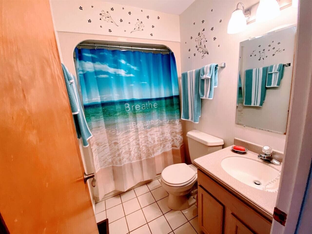 A bathroom with a shower curtain depicting a beach scene, a toilet, a sink, and a mirror.