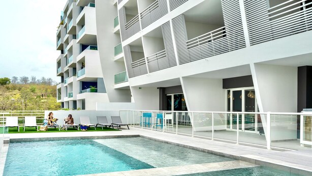 Un hôtel moderne doté d’une piscine, d’un espace extérieur aménagé et d’un immeuble à plusieurs étages avec des balcons.