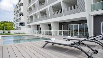 A modern building with a pool and sun loungers.