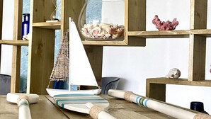 Une étagère en bois sur laquelle se trouve un bol en verre contenant des coquillages, une petite maquette de voilier et un panier tressé.