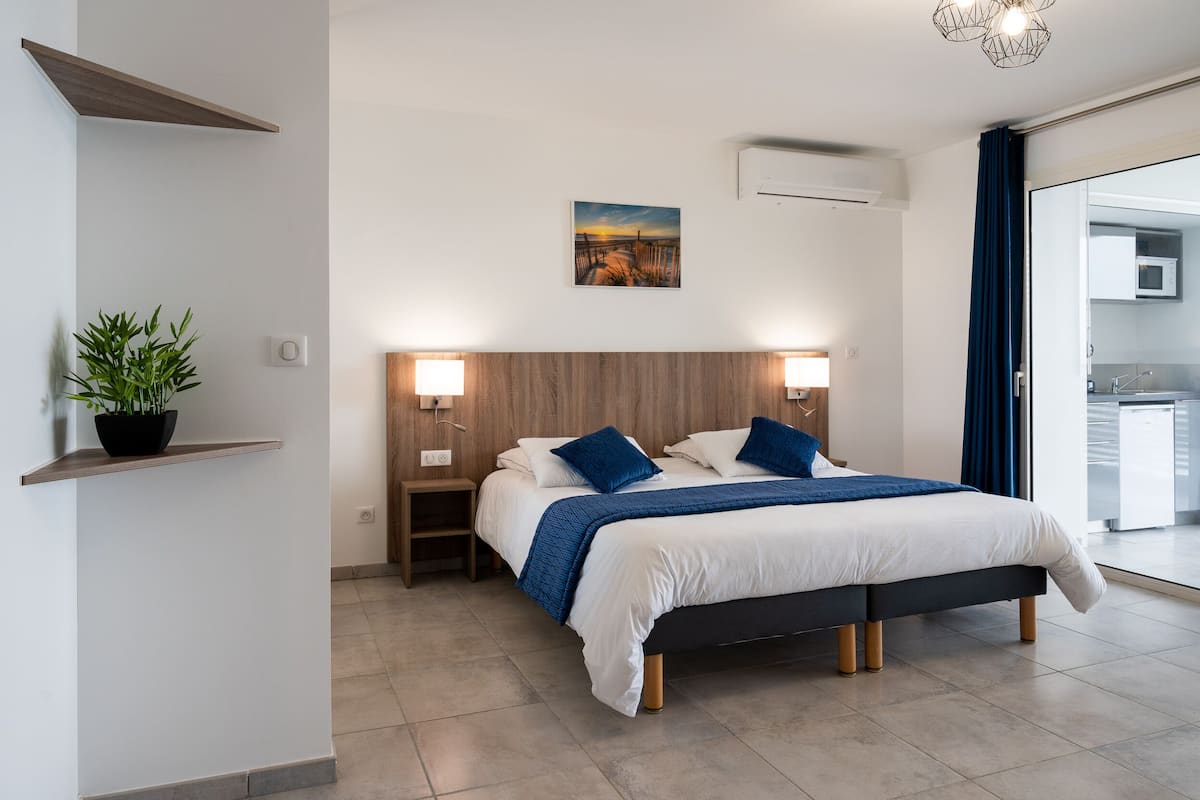 Una habitación de hotel moderna con una cama grande, lámparas de noche, aire acondicionado instalado en la pared y vistas a la cocina a través de una puerta de cristal.