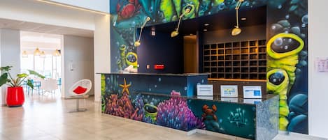 A reception desk with a vibrant underwater mural, a modern seating area, and a visible staircase.