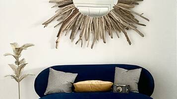 A blue sofa with two pillows and a decorative mirror with a sunburst design on the wall.