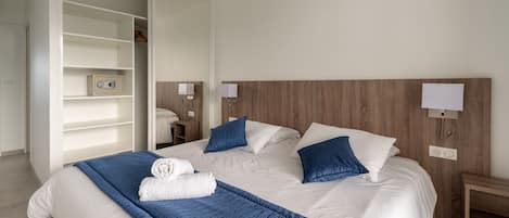 A neatly made bed with a blue blanket and pillows, a wooden headboard, bedside lamps, and a white wardrobe with shelves.