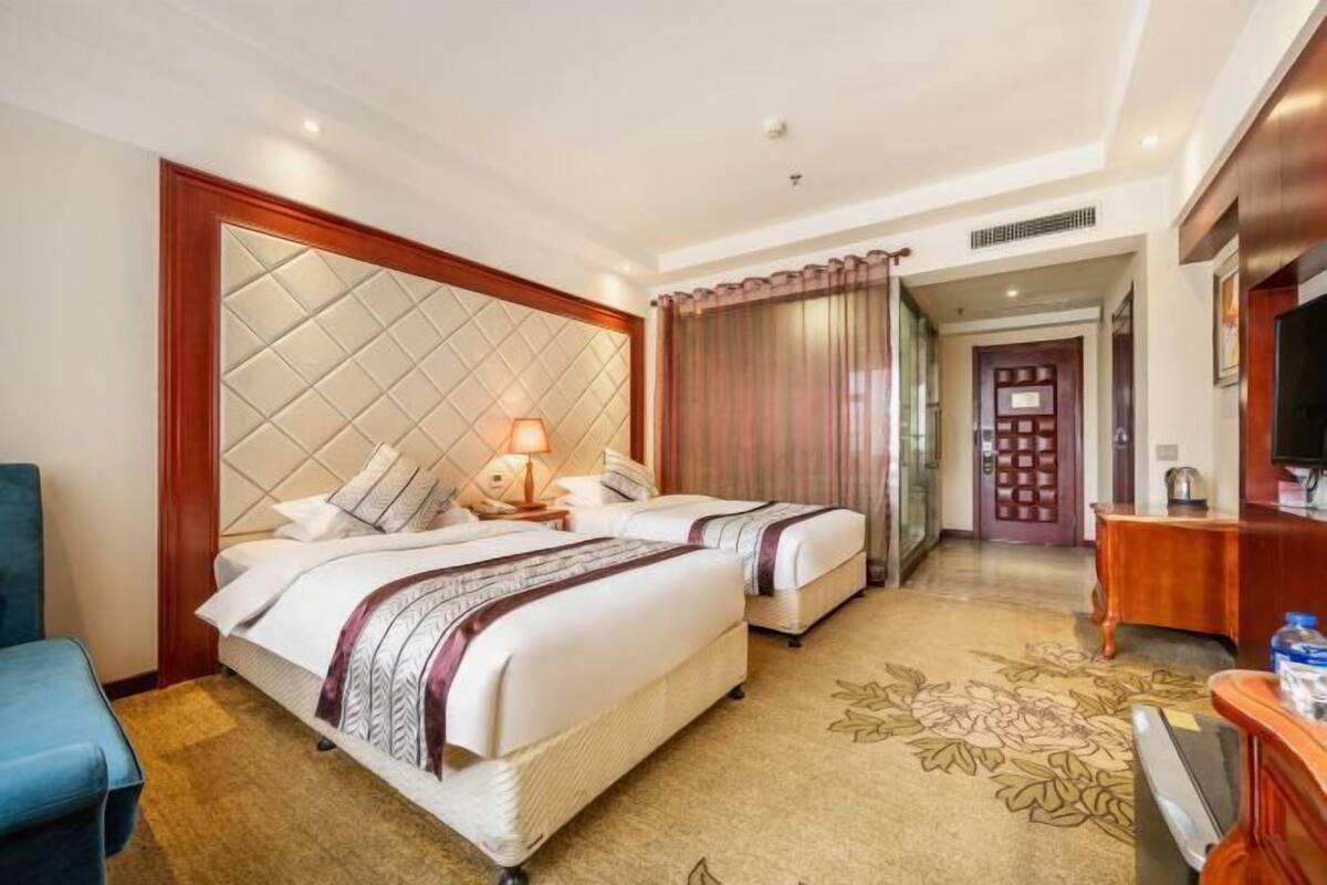 Habitación de hotel con dos camas, un escritorio, una silla y un televisor.