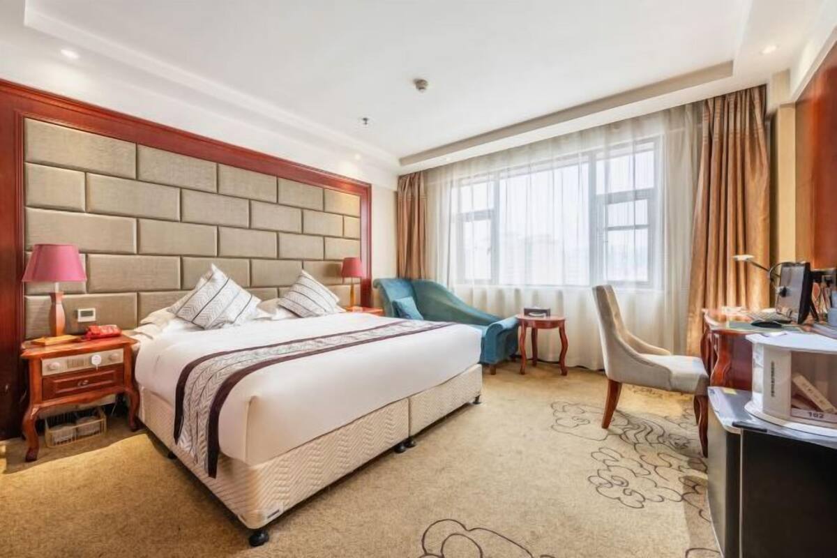 Una habitación de hotel con una cama grande, dos mesitas de noche, un escritorio, una silla y una ventana con cortinas.