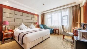 A hotel room with a large bed, two bedside tables, a desk, a chair, and a window with curtains.
