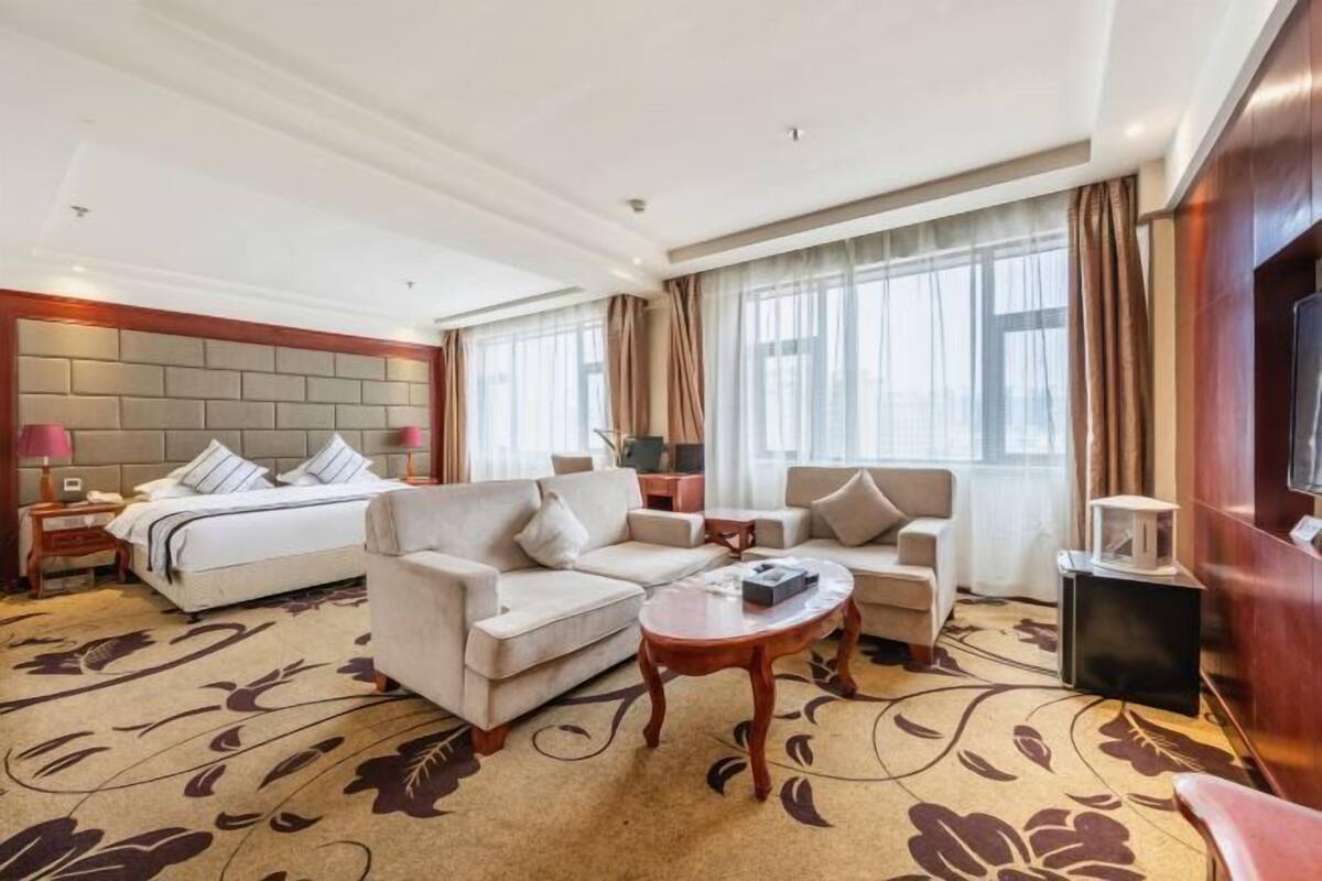 Habitación de hotel con una cama, dos sofás, una mesa de centro y un televisor.