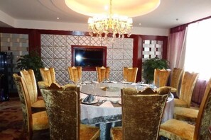 Un coin repas avec une table ronde, des chaises, un lustre et un téléviseur fixé au mur.