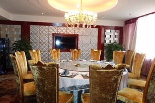Uma sala de jantar com uma mesa redonda, cadeiras, um lustre e uma televisão na parede.