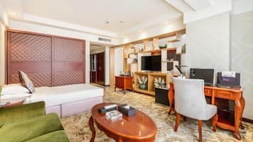 A hotel room with a bed, a green sofa, a wooden coffee table, a desk with a computer, and a TV.