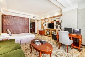 A hotel room with a bed, a green sofa, a wooden coffee table, a desk with a computer, and a TV. - Qin Hai International Hotel (Baiyin)