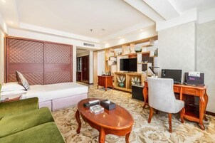 Una habitación de hotel con una cama, un sofá verde, una mesa de centro de madera, un escritorio con una computadora y un televisor.