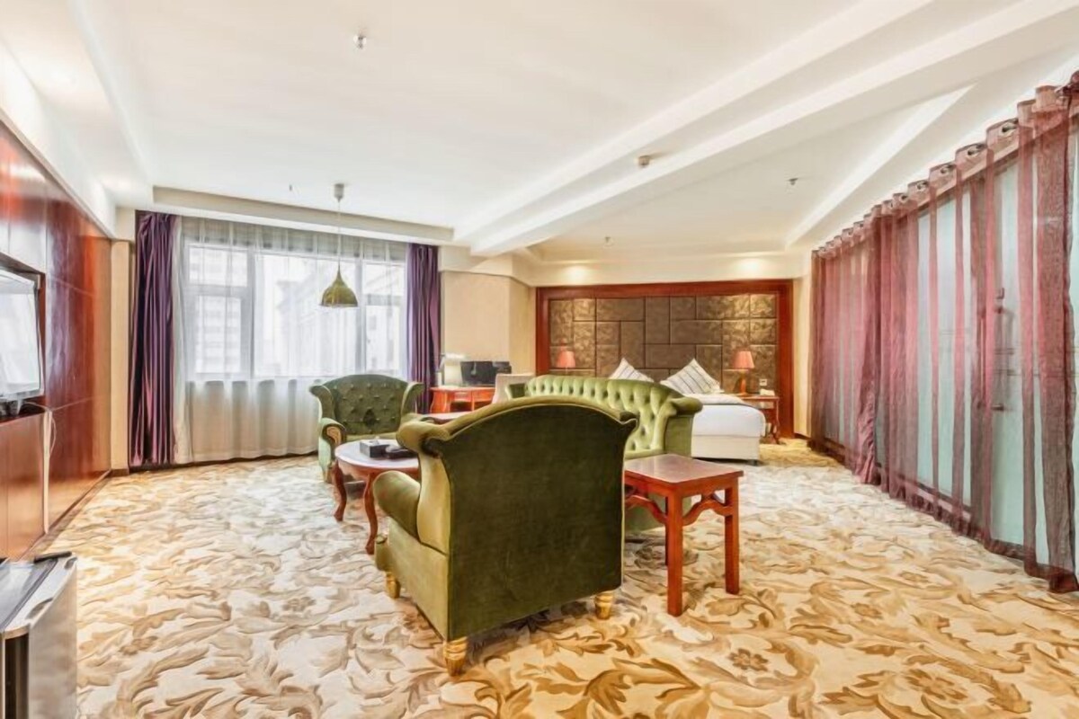 A hotel room with a green armchair, a sofa, a small table, and a bed.