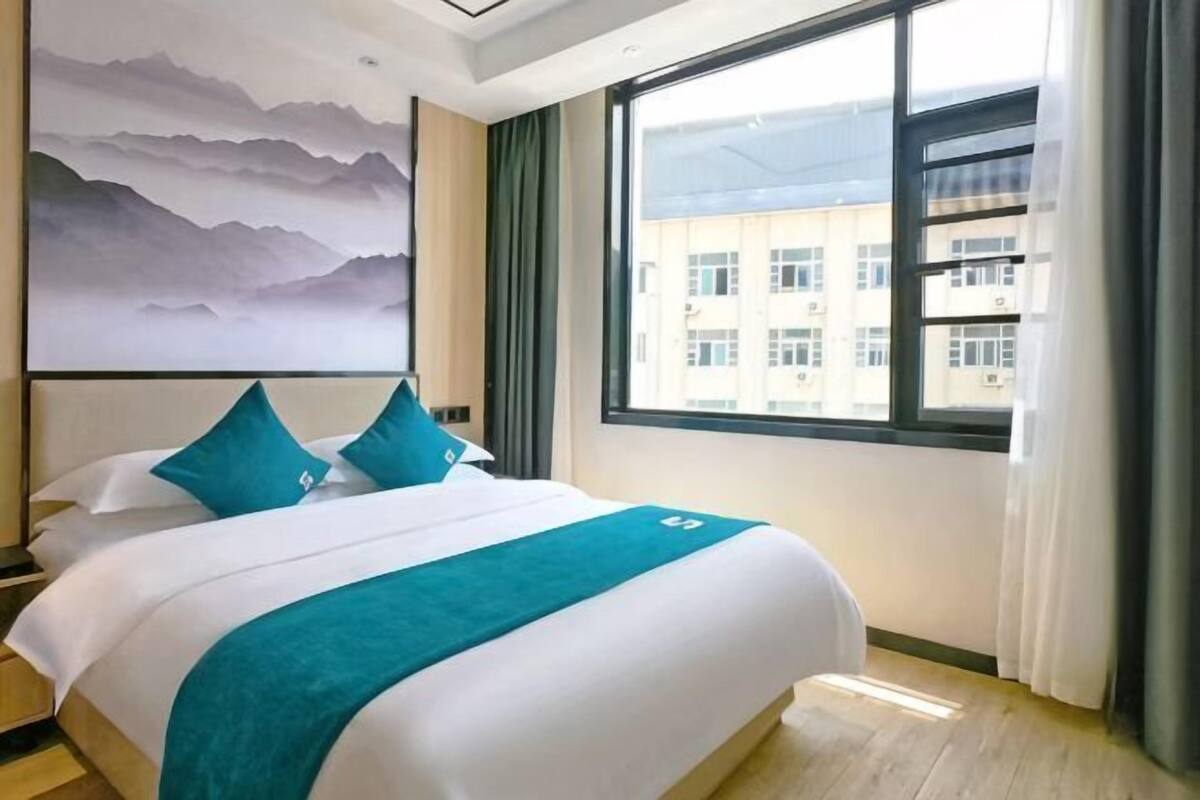 A hotel room with a large bed, a view of buildings, and a painting on the wall.