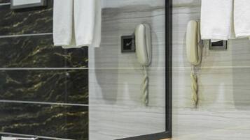 A hotel room with a marble wall, two phones, and a towel rack.