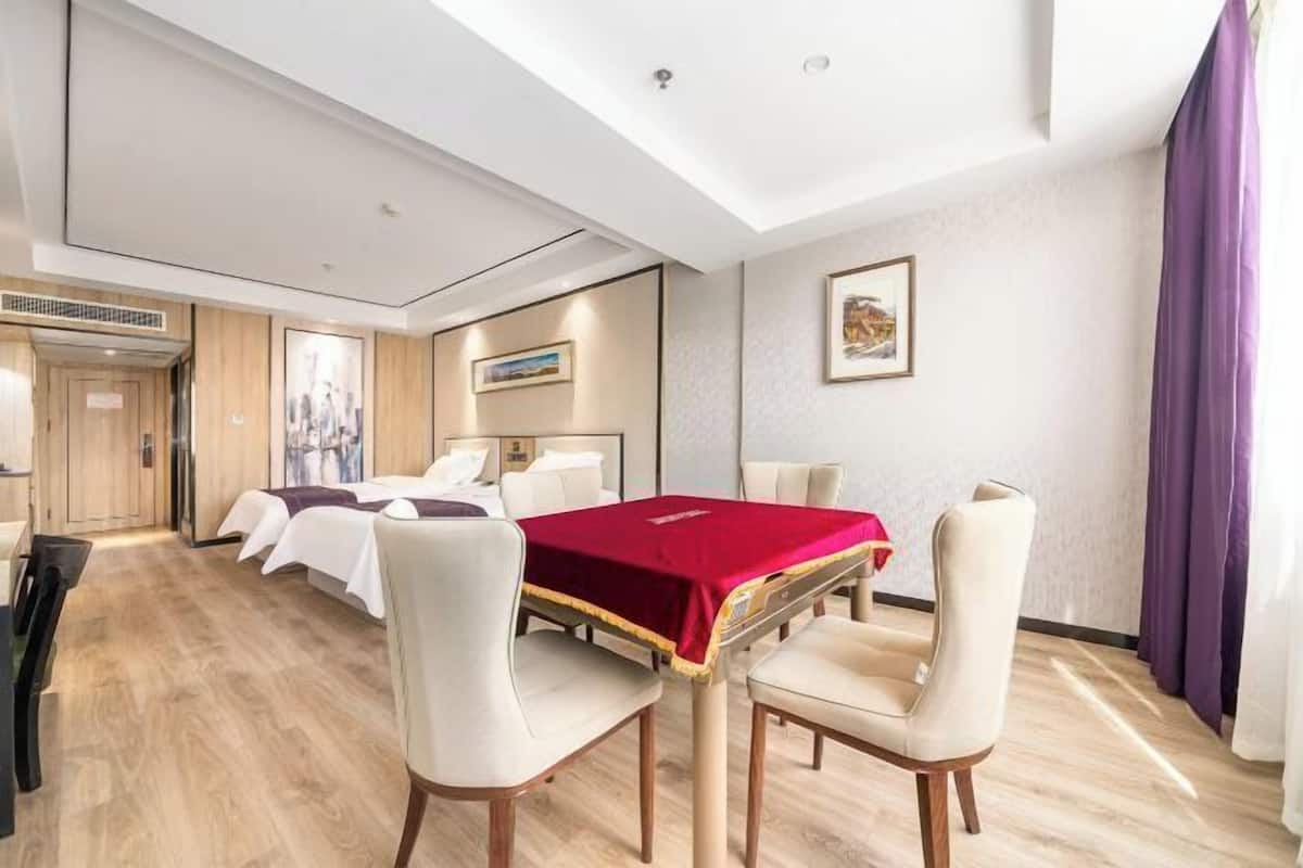 A hotel room with a bed, two bedside tables, a desk with a chair, and a dining table with four chairs.