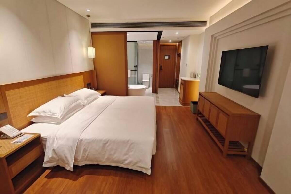 A hotel room with a large bed, a TV, a wooden cabinet, and a bathroom visible through an open door.